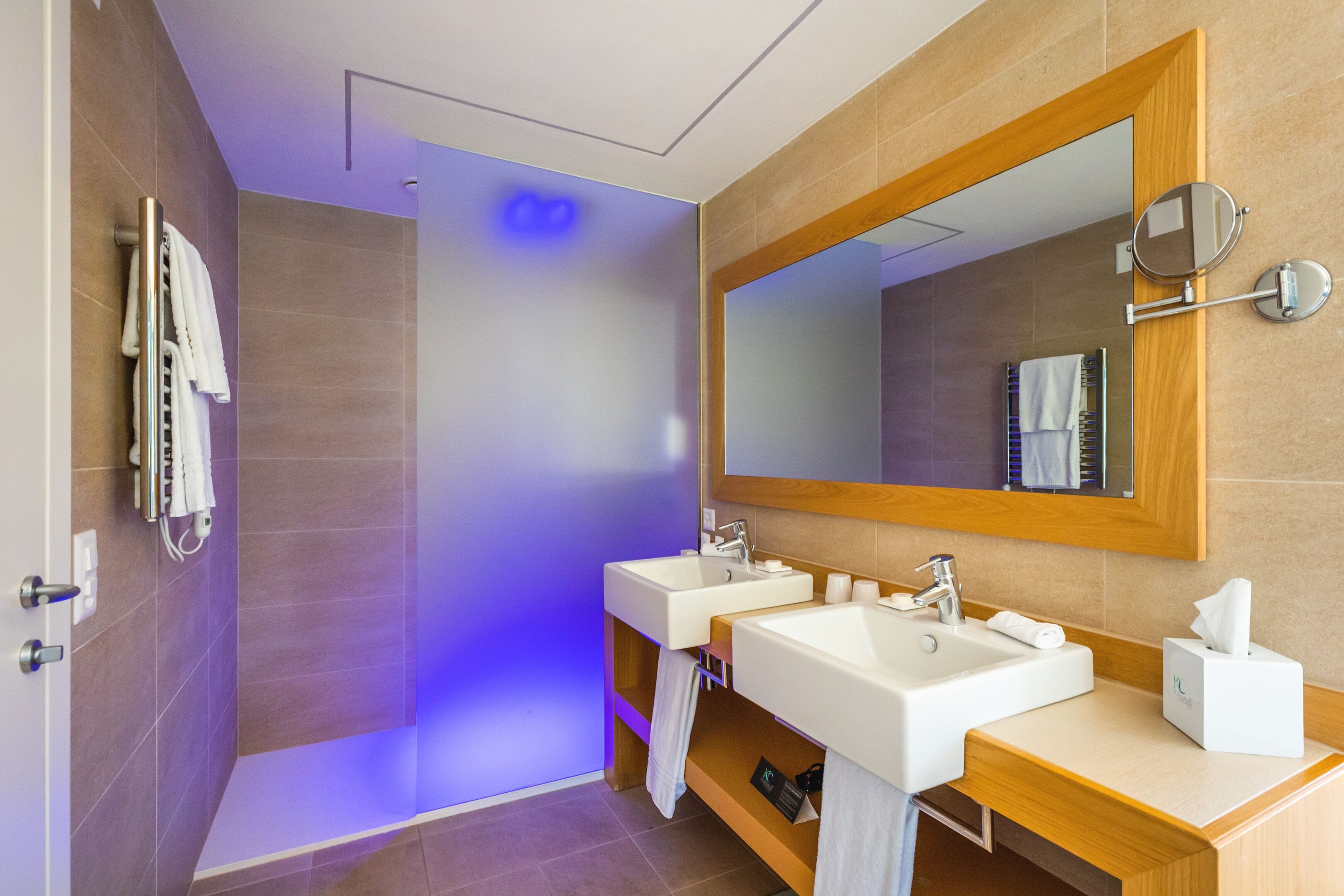 A modern bathroom with two sinks, a large mirror, and a shower area.
