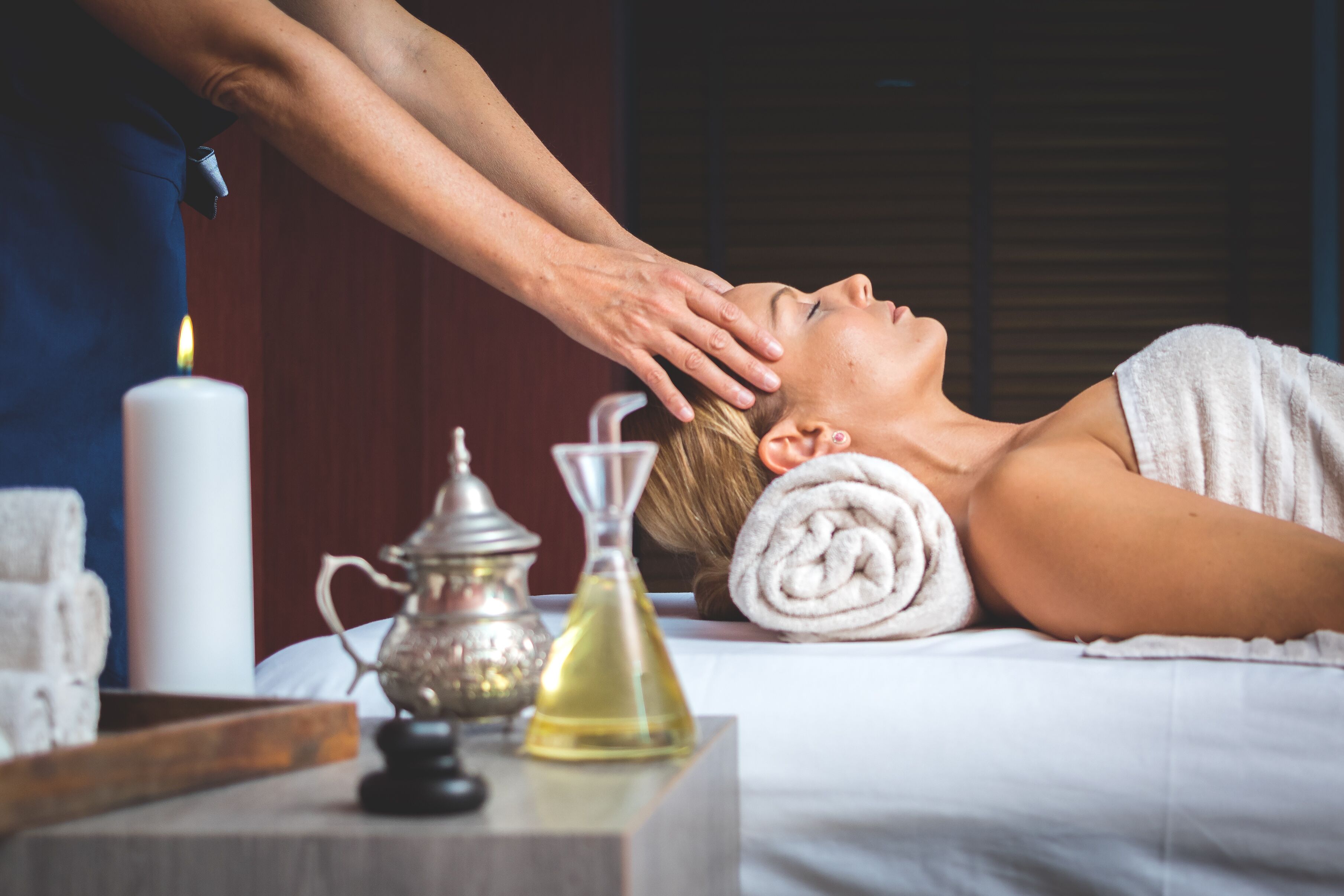 Une personne reçoit un massage dans une pièce où se trouvent une bougie, un diffuseur et une bouteille d’huile sur une table.