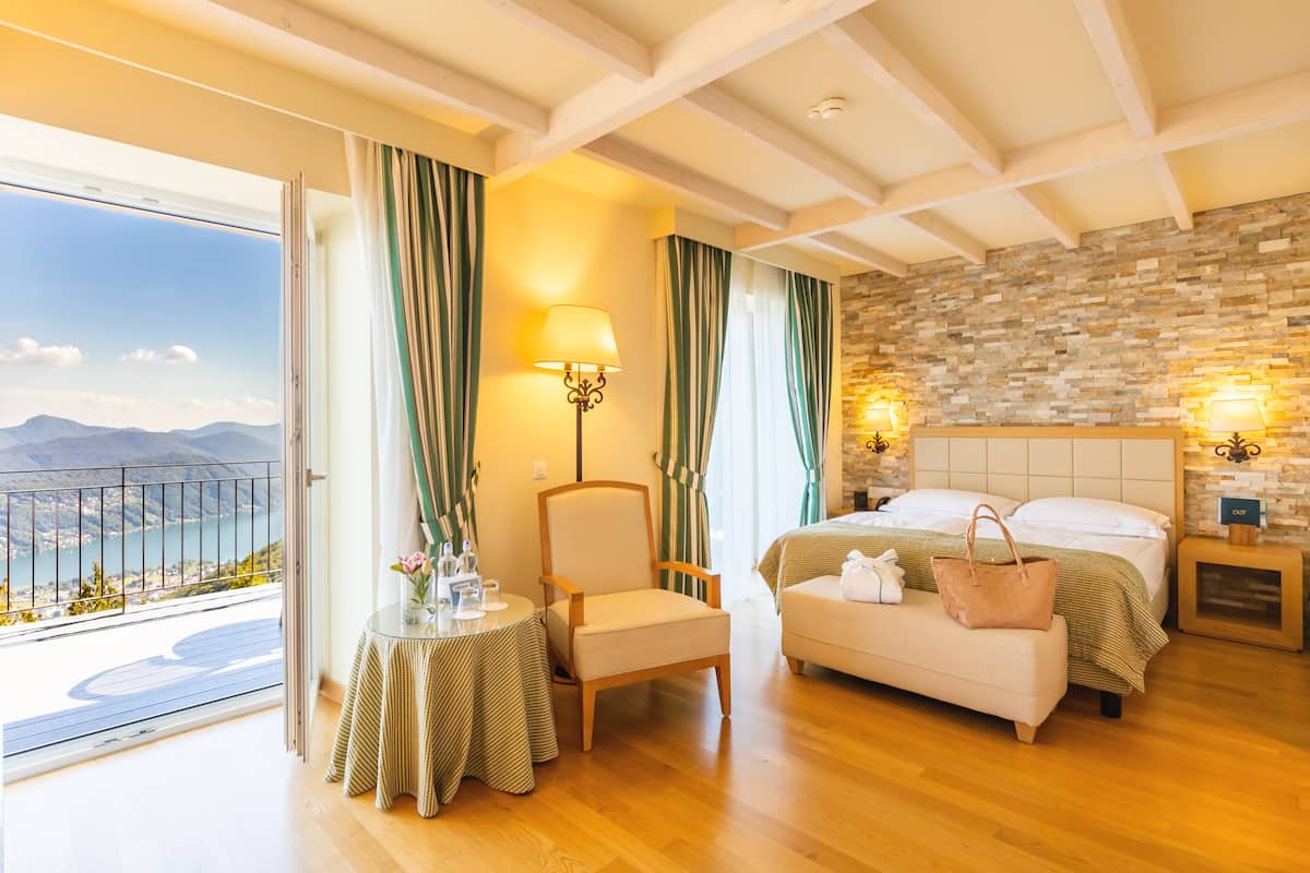 A hotel room with a balcony, a bed, a chair, a table, and a nightstand.