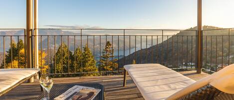 A balcony with a wicker table, two lounge chairs, a glass of wine, and a magazine.