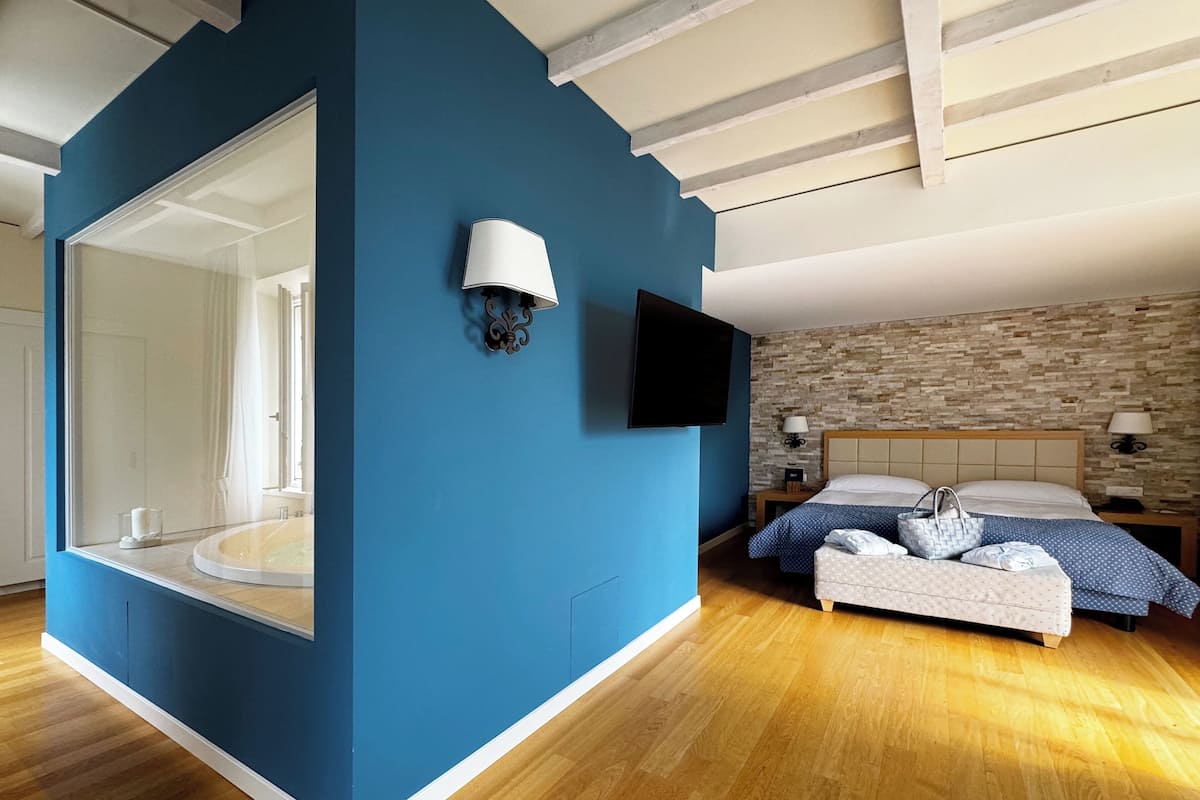 A bedroom with a large mirror, a bed with a blue and white polka dot duvet, a wooden headboard, and a stone-patterned wall.
