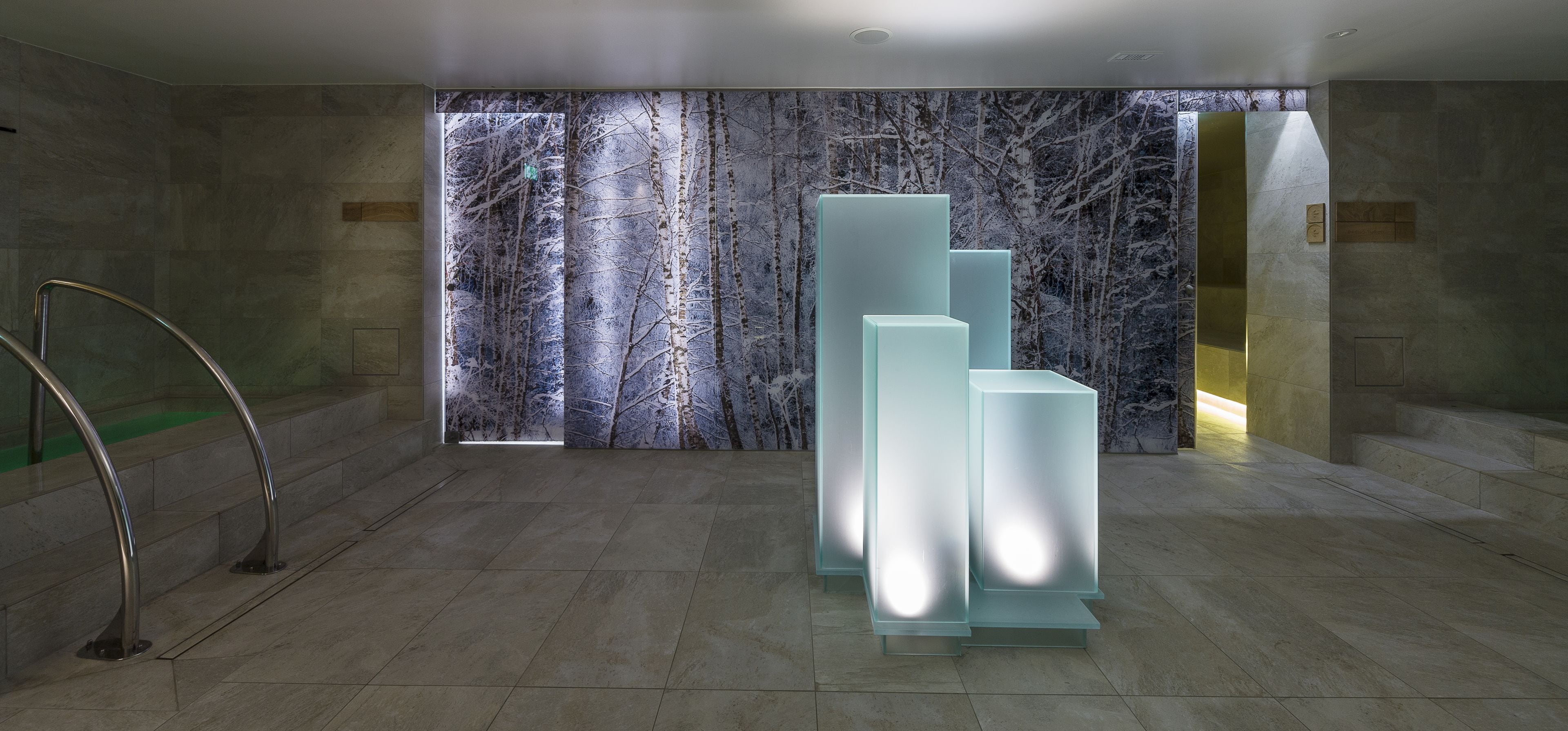 A modern lobby with a large wall mural, a staircase, and a series of illuminated panels.