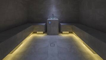 Ein modernes, schwach beleuchtetes Badezimmer mit einem zentralen Waschbecken, gefliesten Wänden und Fußbodenheizung.