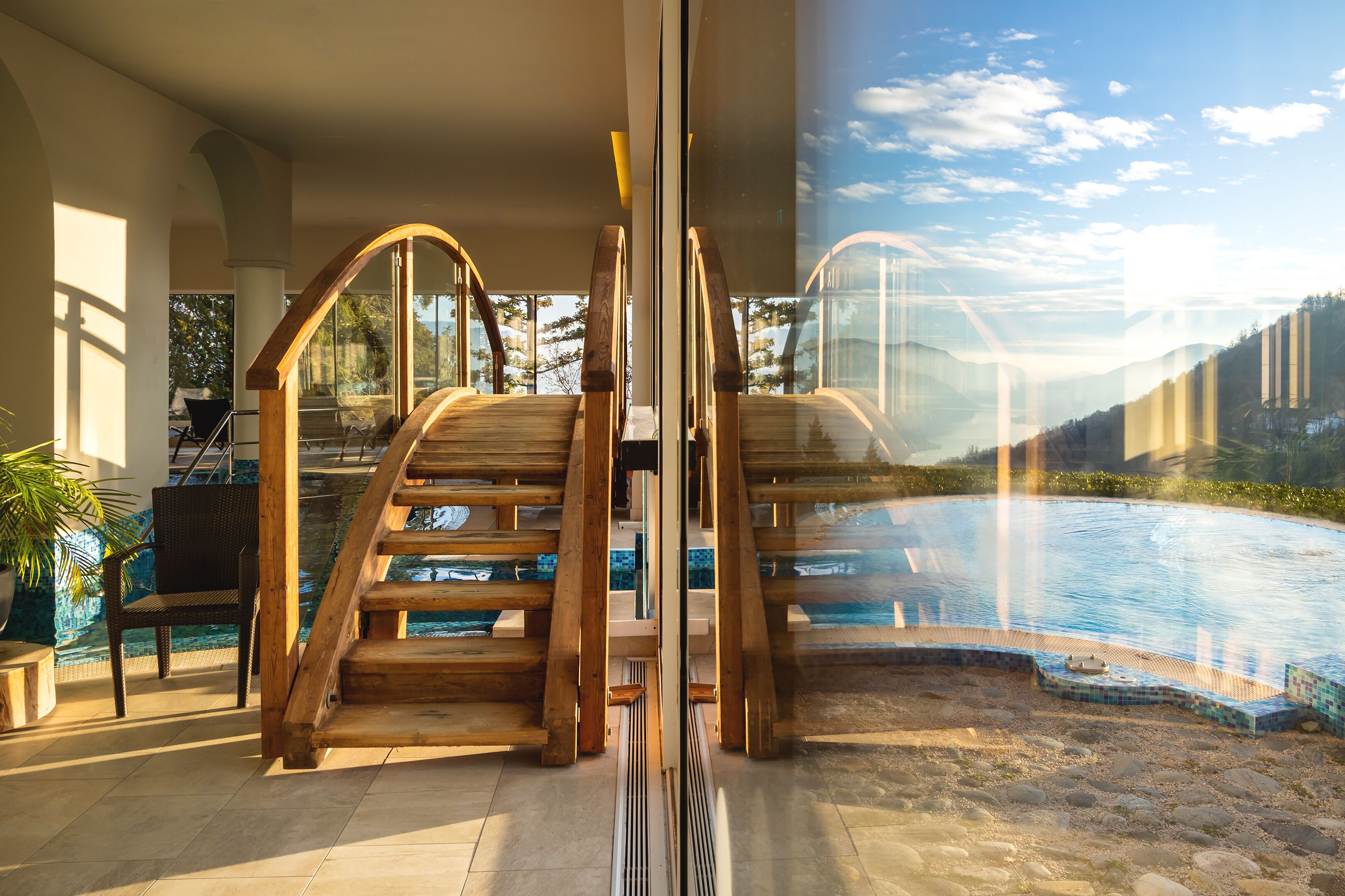 Un área de piscina interior moderna con escalones de madera y una barrera de vidrio.