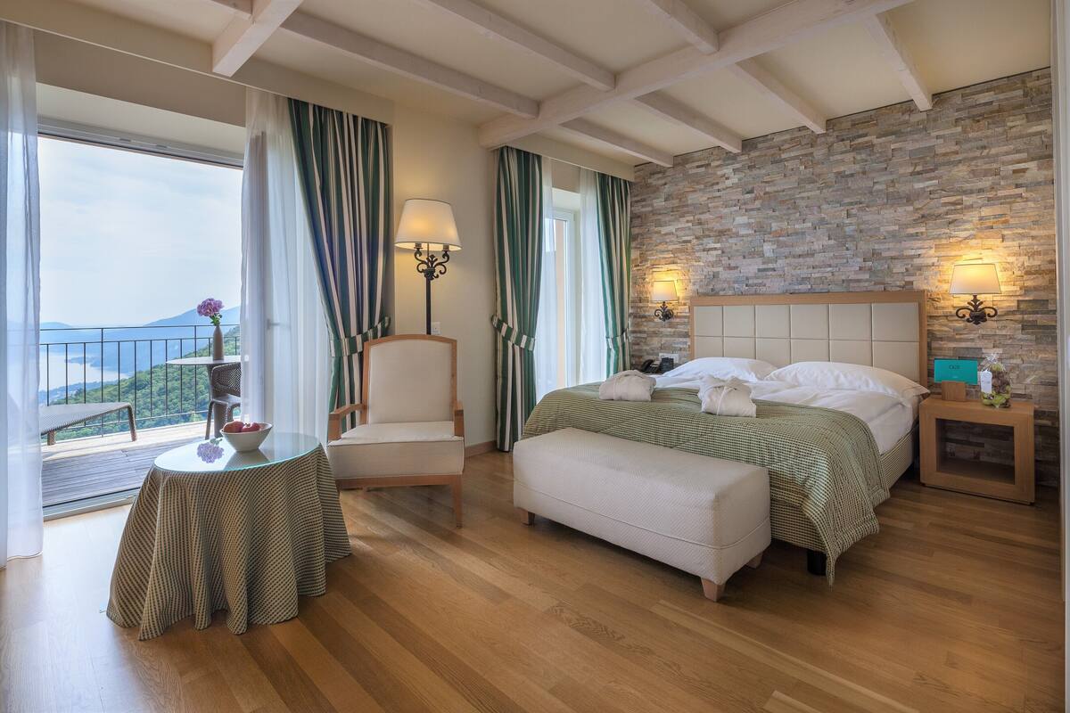 A bedroom with a stone wall, a bed, a chair, a table, and a view of the outdoors.