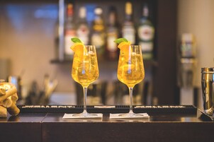 Dos vasos de una bebida amarilla con rodajas de naranja y hojas de menta sobre una barra.