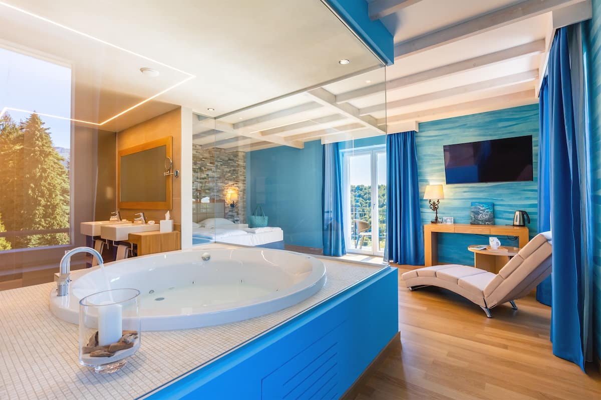 A modern bathroom with a large bathtub, a glass shower enclosure, and a seating area with a TV.