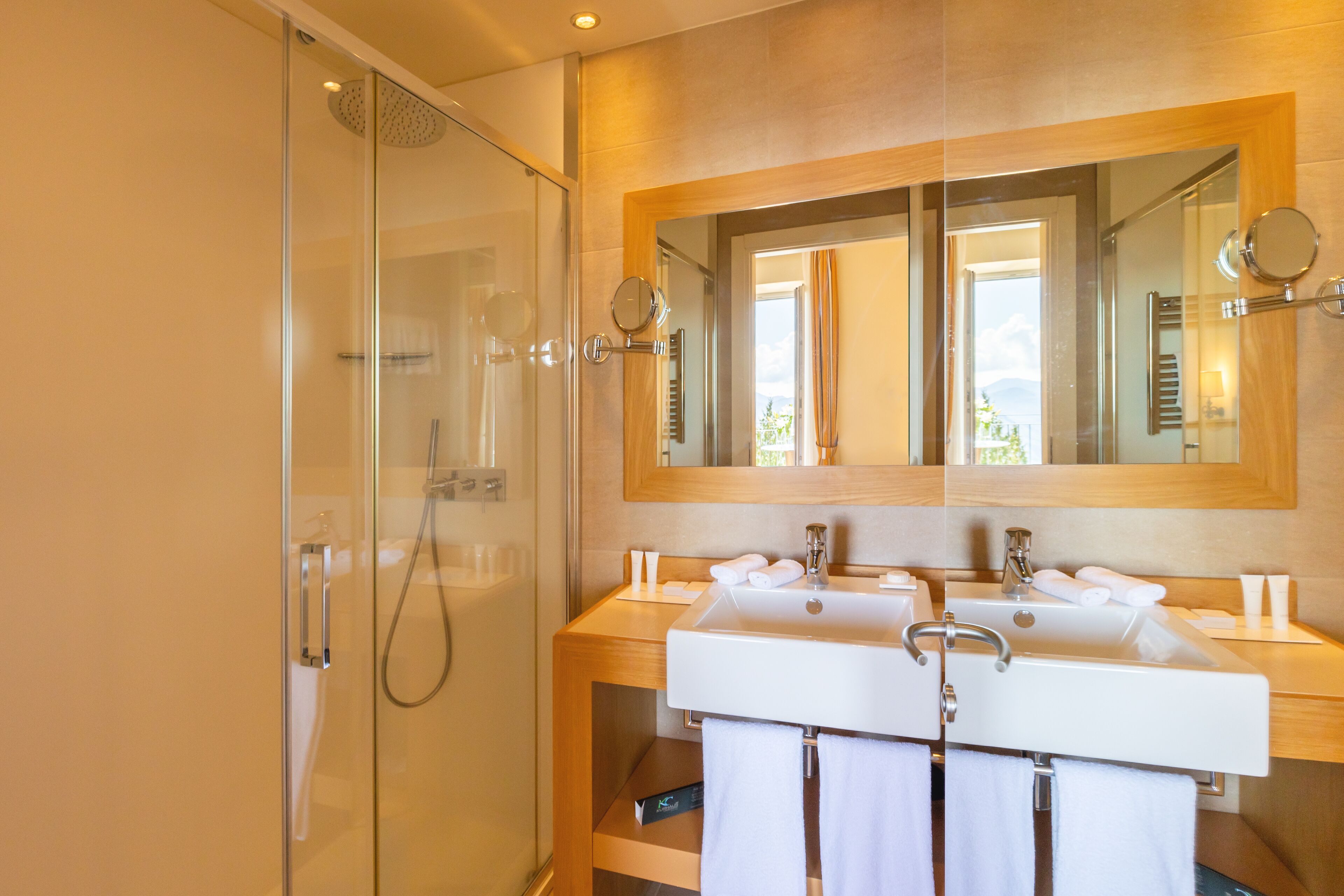 Un baño moderno con cabina de ducha de vidrio, dos lavamanos y un espejo grande.