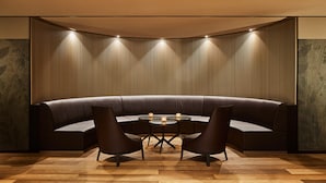 A modern lounge area with a curved sofa, two armchairs, and a small round table with candles. - Hotel Uzwil (Uzwil)