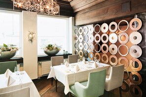 A dining area with round mirrors on the wall, a chandelier, and a window with a view.