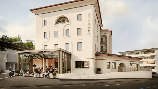 A modern hotel with a central atrium, outdoor seating area, and a glass facade. - Hotel Uzwil (Uzwil)