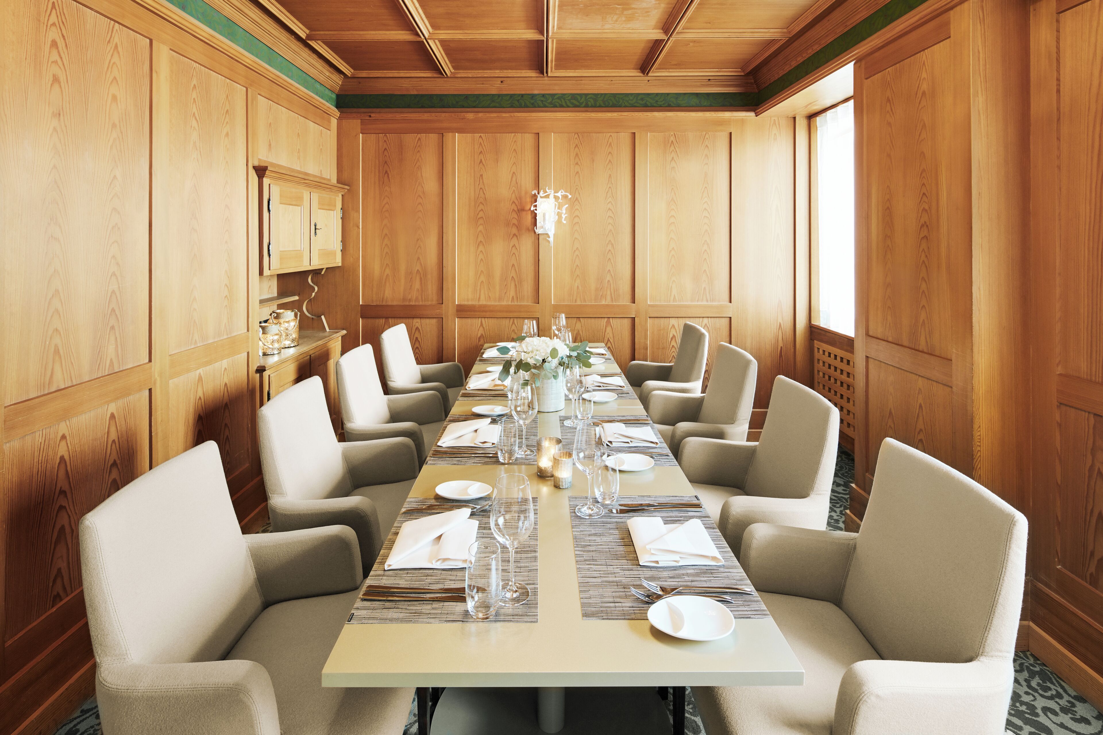 Une salle de conférence avec une longue table préparée pour une réunion, entourée de chaises, avec des lambris en bois sur les murs et un lustre au plafond.