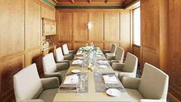 Une salle de conférence avec une longue table préparée pour une réunion, entourée de chaises, avec des lambris en bois sur les murs et un lustre au plafond.
