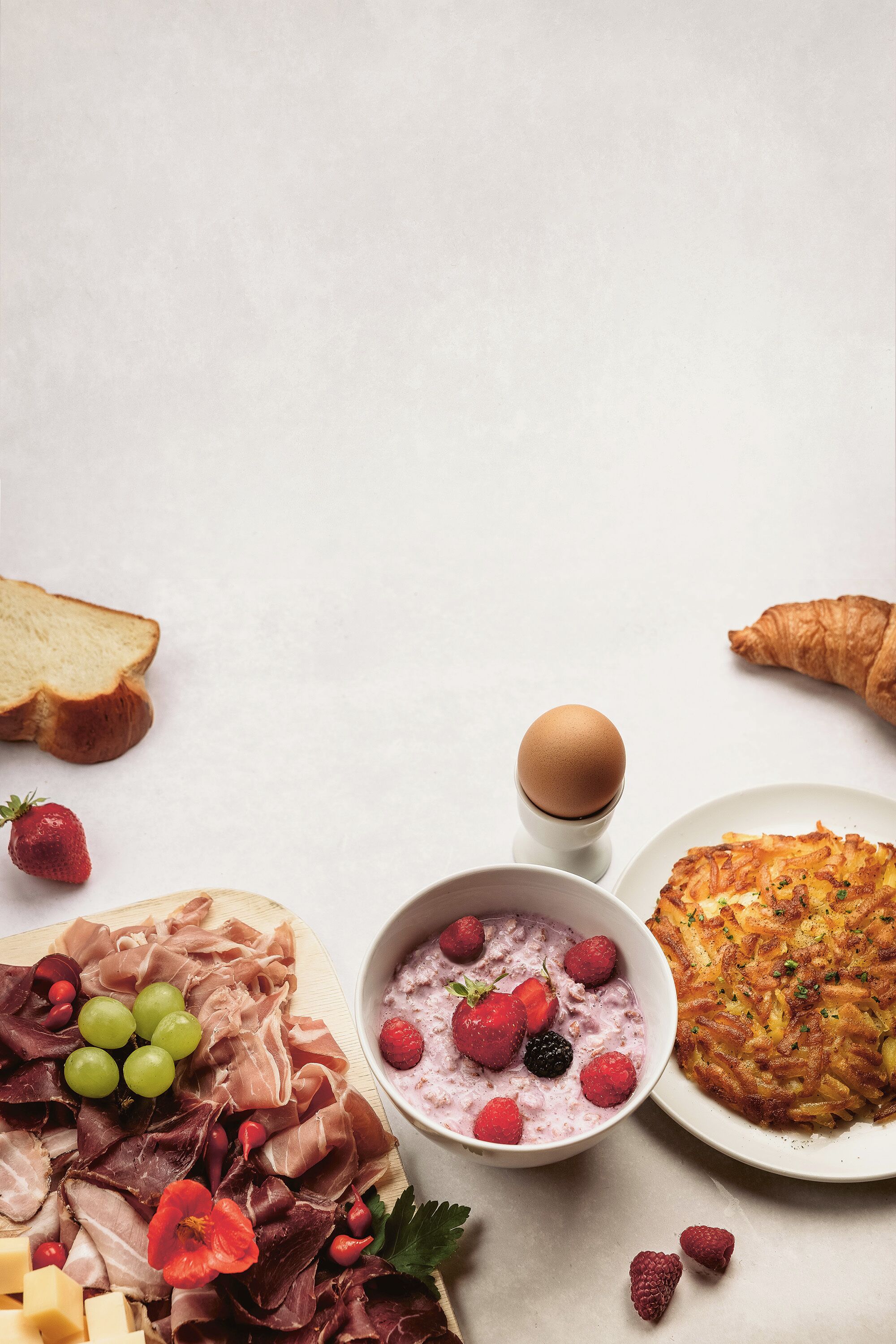 A breakfast spread with various foods including bread, eggs, a croissant, a fruit bowl, and a cheese platter.