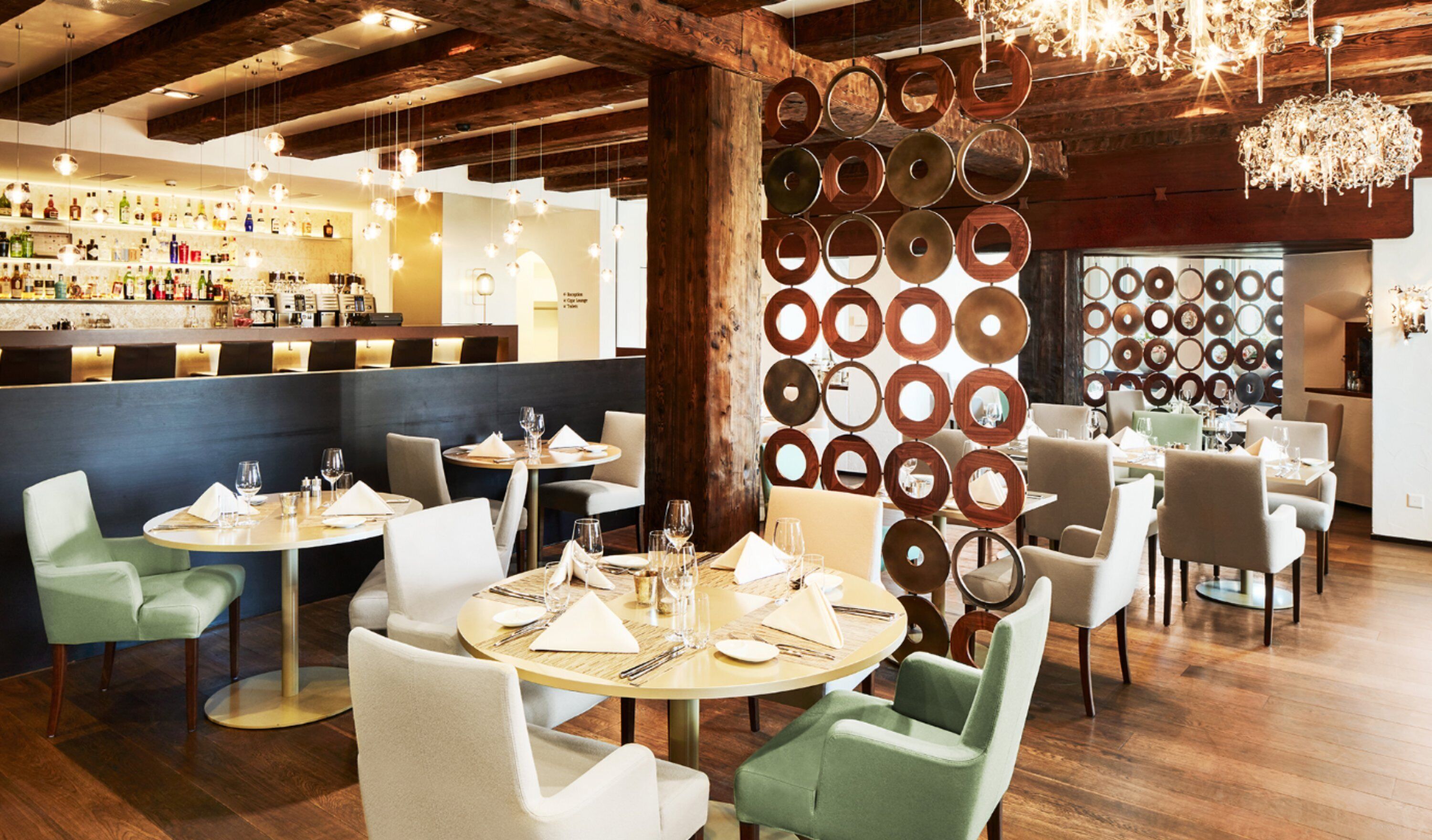 Un restaurant avec des tables rondes, des chaises vertes et un bar où sont exposées des bouteilles.