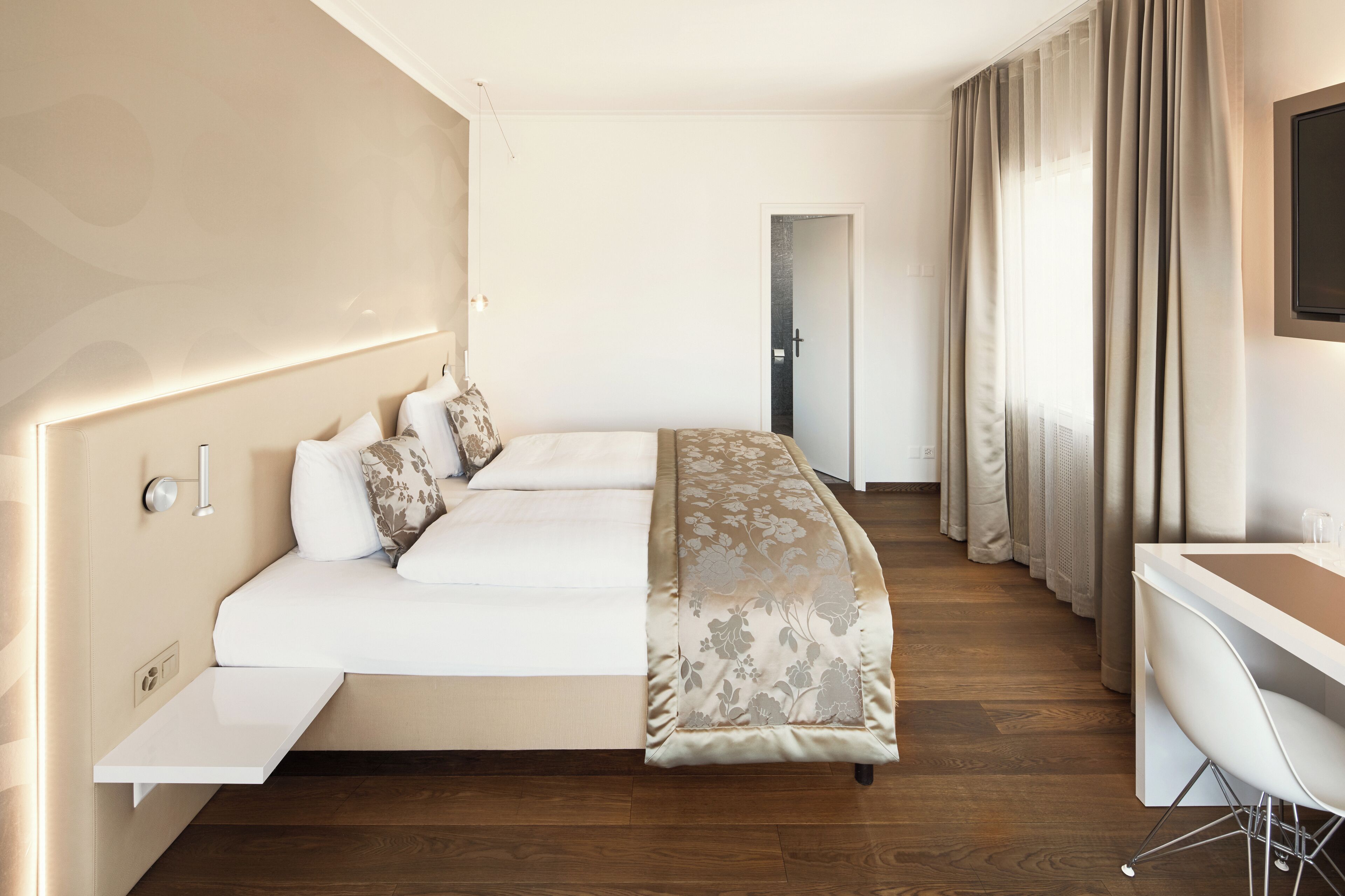 A hotel room with a bed, bedside table, desk, and chair.