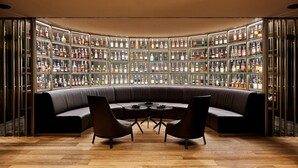 A modern bar area with a curved seating arrangement, a wooden floor, and a wall of neatly organized liquor bottles. - Hotel Uzwil (Uzwil)