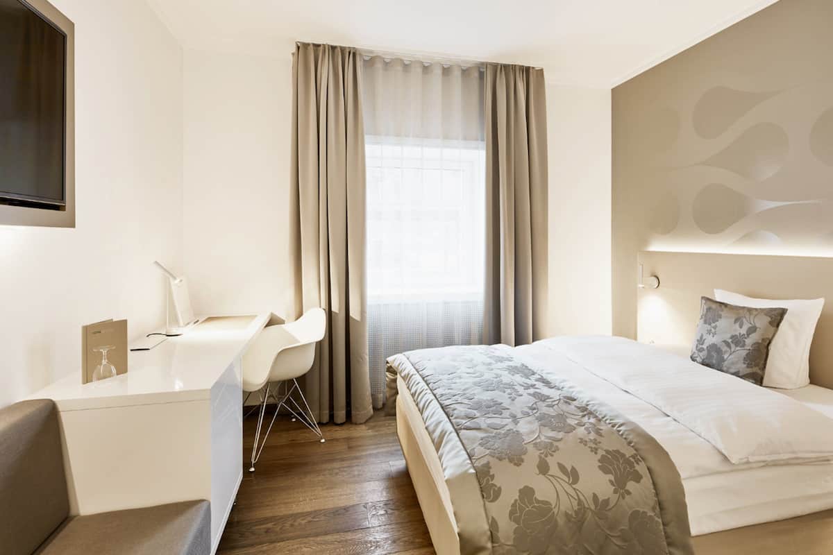 A modern hotel room with a bed, a desk, and a chair.