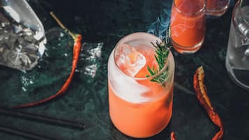 A cocktail with a garnish, ice, and a dark background with scattered items.