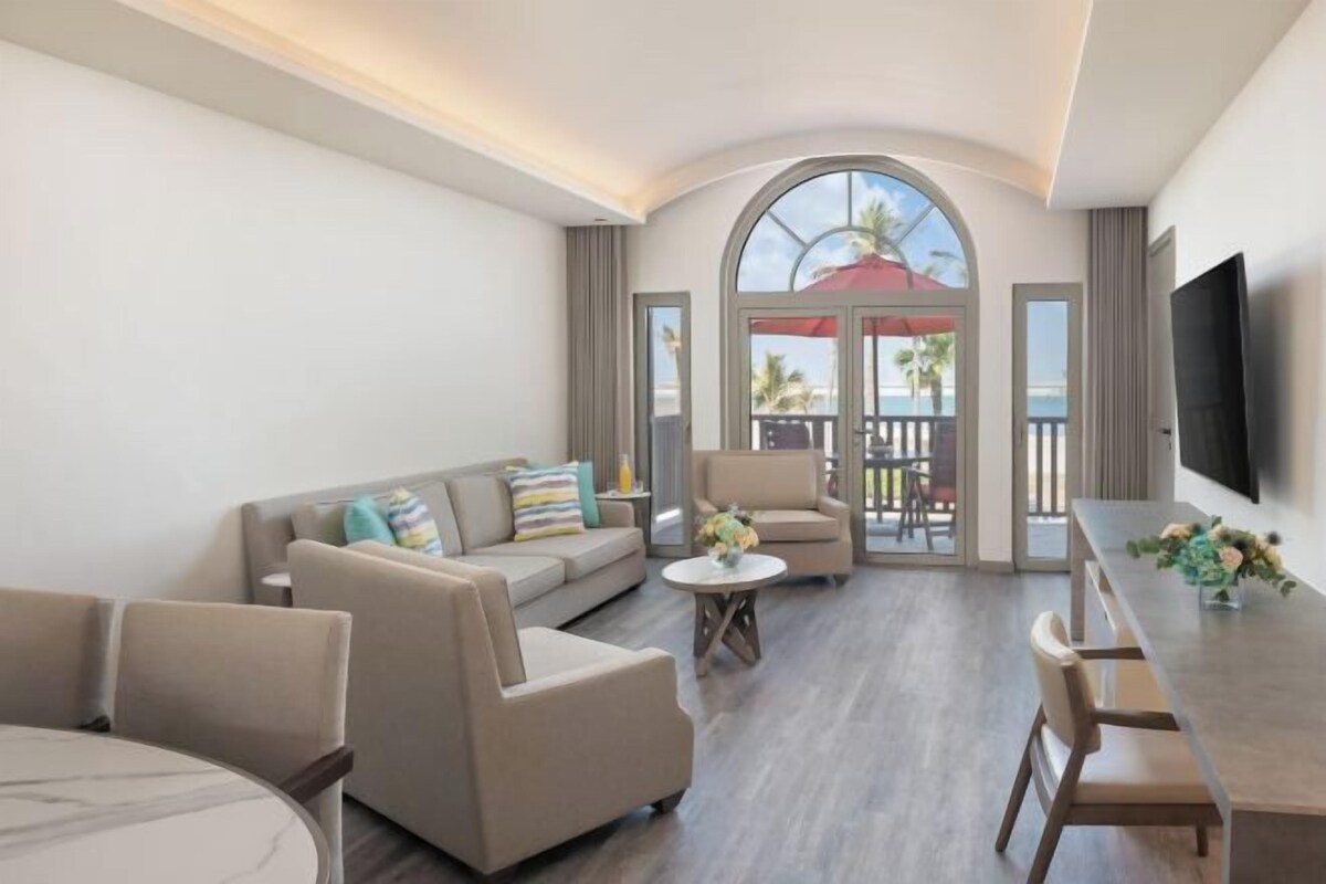 A spacious living area with a sofa, chairs, a dining table, and a TV.