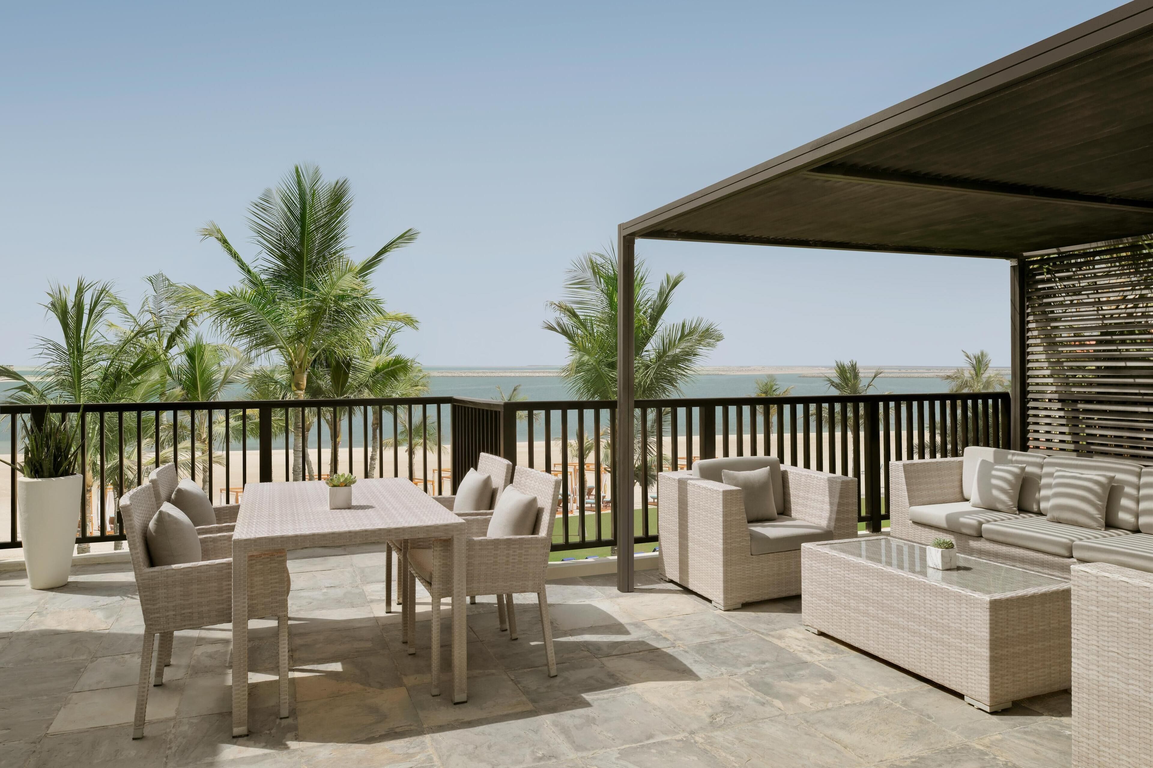 Een terras buiten met rieten meubilair, een tafel en uitzicht op het strand.