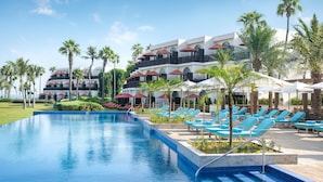 A swimming pool with lounge chairs and umbrellas, surrounded by palm trees and a multi-story building with balconies. - JA Palm Tree Court, Dubai (Dubai)