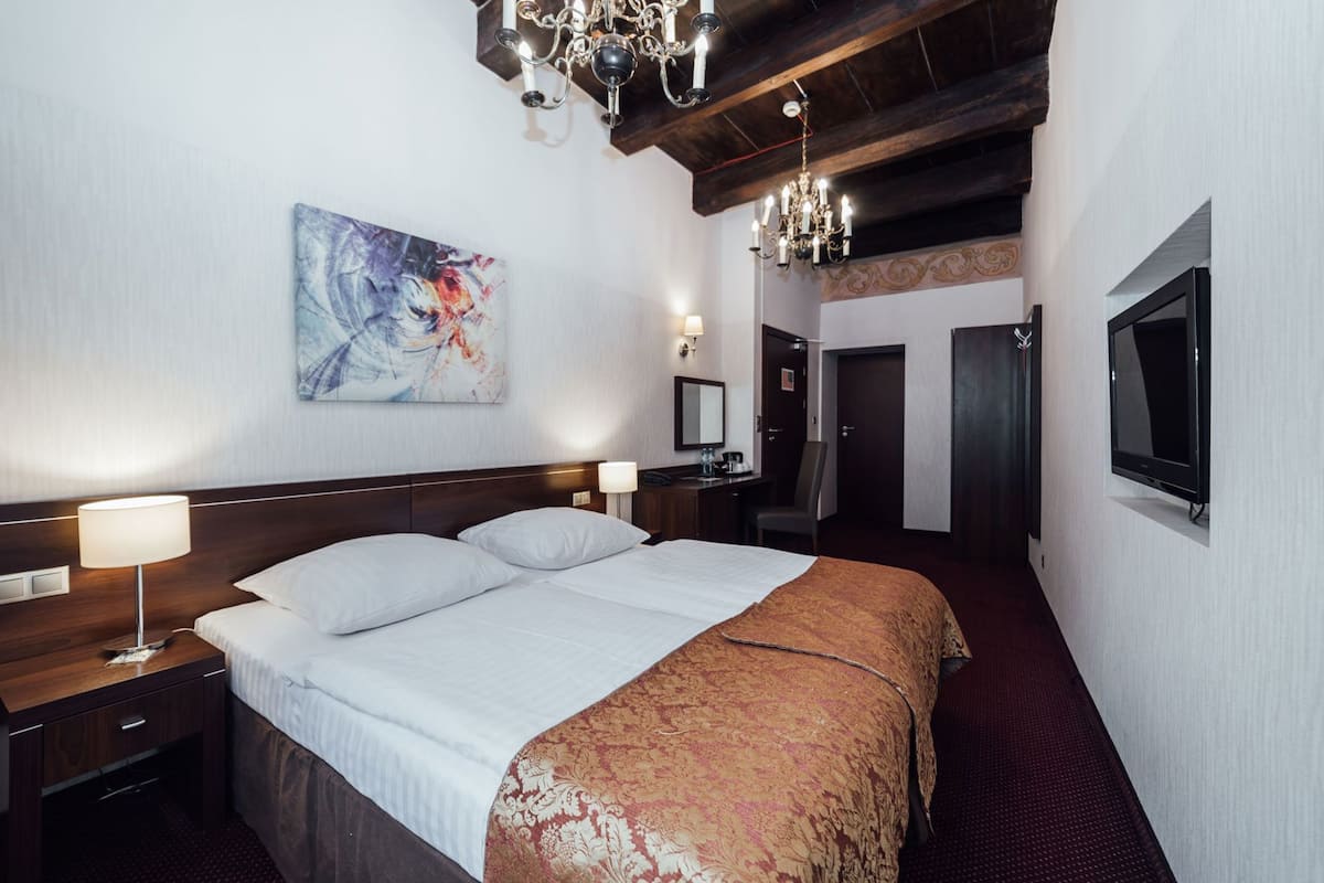 Habitación de hotel con una cama grande, lámparas de noche, un cuadro en la pared, televisión y un candelabro.