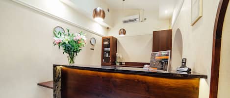 A reception desk with a wooden finish, a clock, a vase with flowers, and a phone.