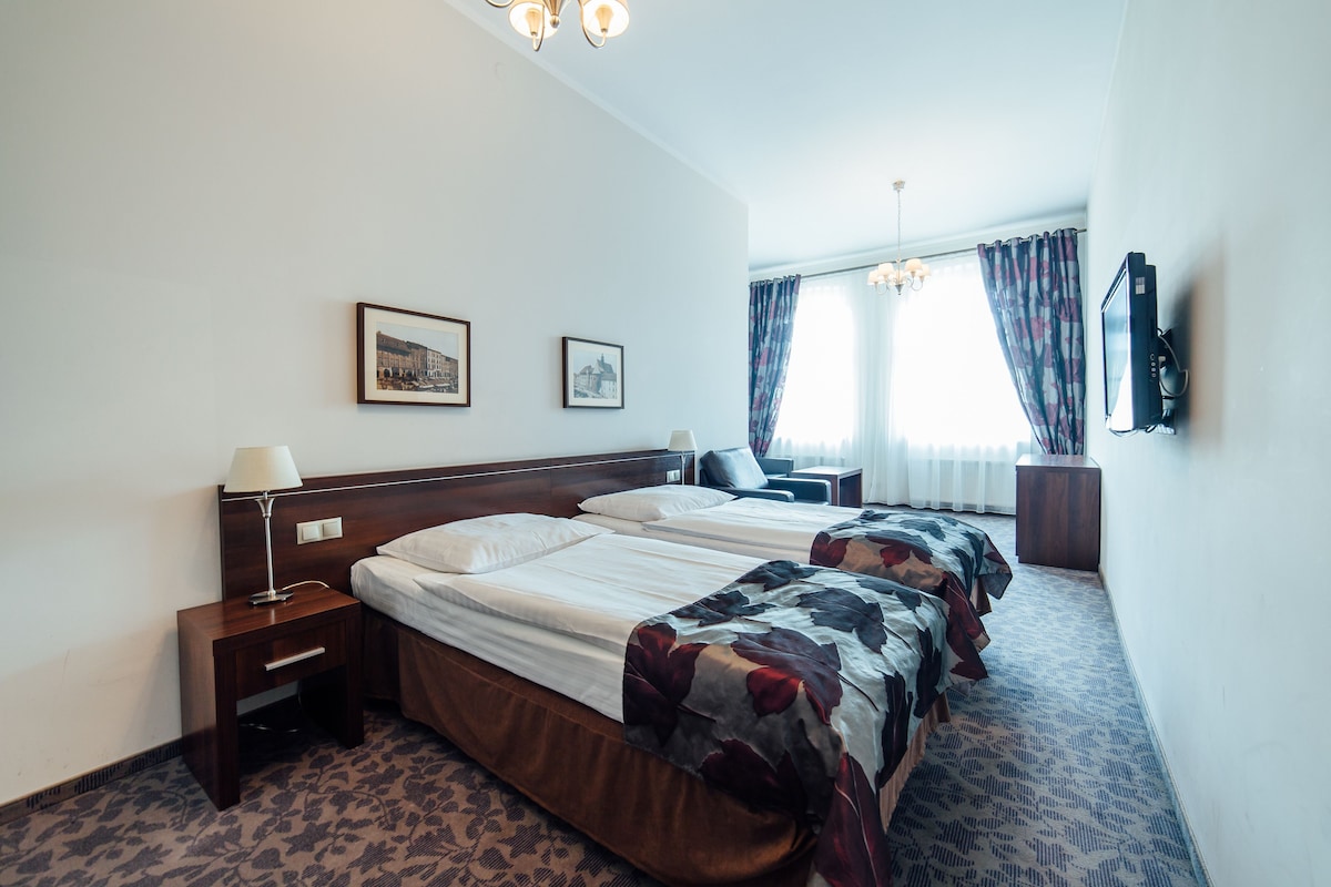 A hotel room with two beds, a desk, a chair, a TV, and a window with curtains.