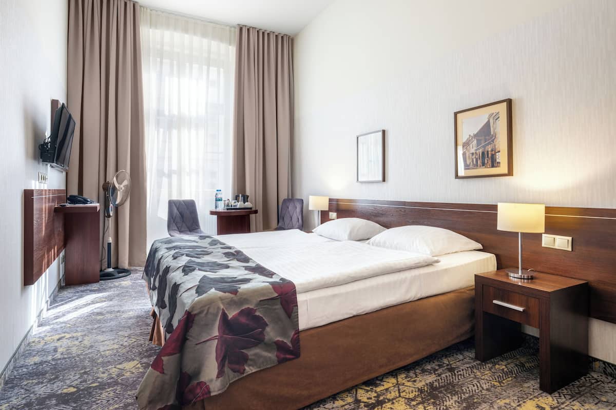 Habitación de hotel con cama, dos mesitas de noche, un escritorio con silla, televisión y un ventanal con cortinas.