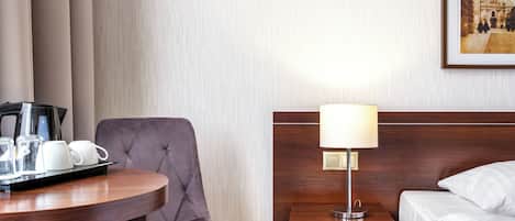 Habitació d'hotel amb un llit, una taula de nit amb una làmpada, una cadira, una taula petita amb una bandeja de menjar i una fotografia encadrada a la paret.