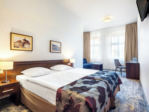 A hotel room with a large bed, two bedside tables, a desk, a chair, and a TV. - Hotel Rezydent (Kraków)