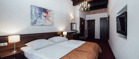 Une chambre d’hôtel avec un grand lit, deux tables de chevet, un bureau, une chaise, une télévision et un lustre.