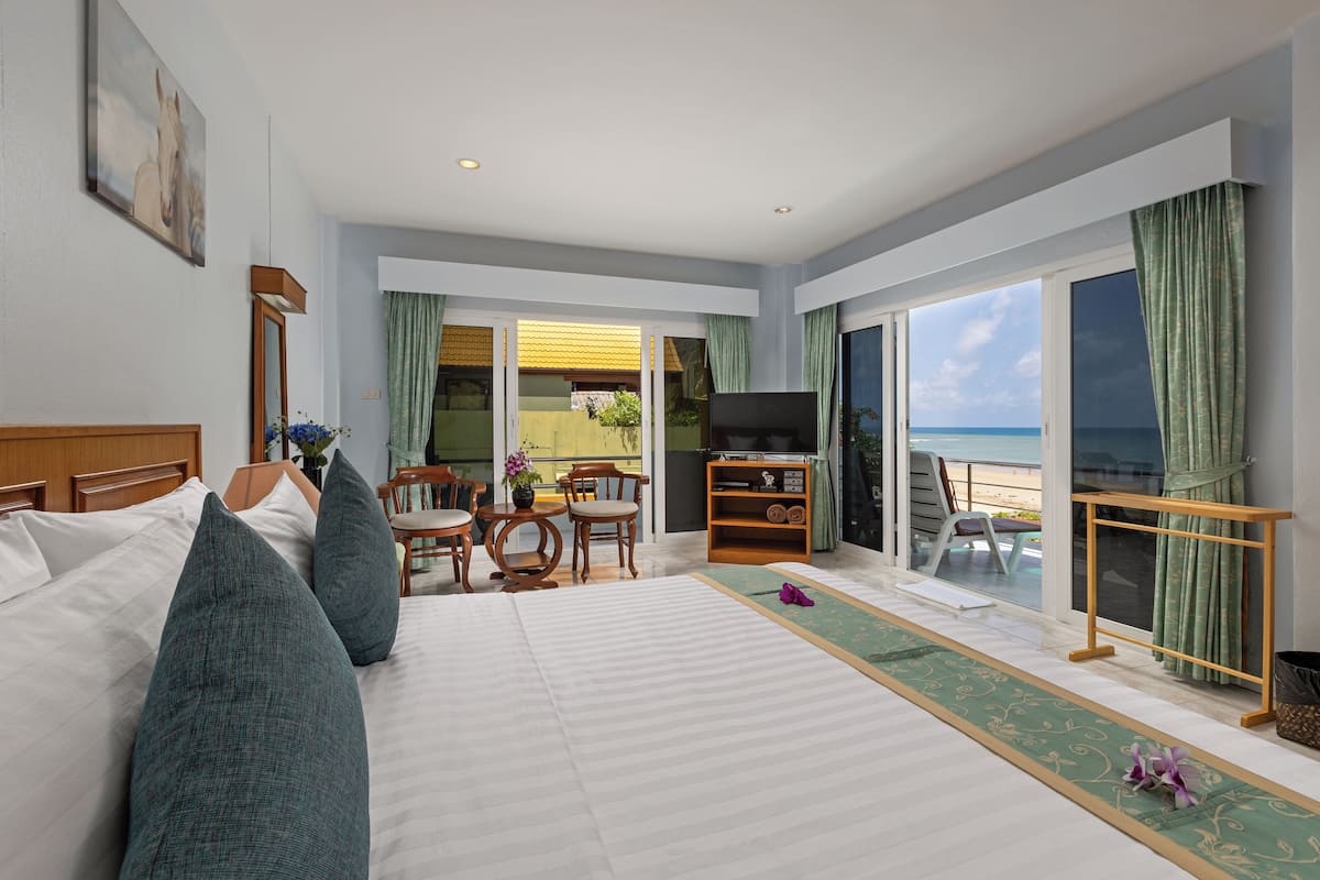 A hotel room with a bed, a TV, a seating area with chairs, a small table, and a view of the ocean through large windows.
