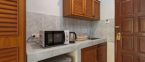 Una cocina compacta con microondas, hervidor y tostadora sobre una encimera de cristal.