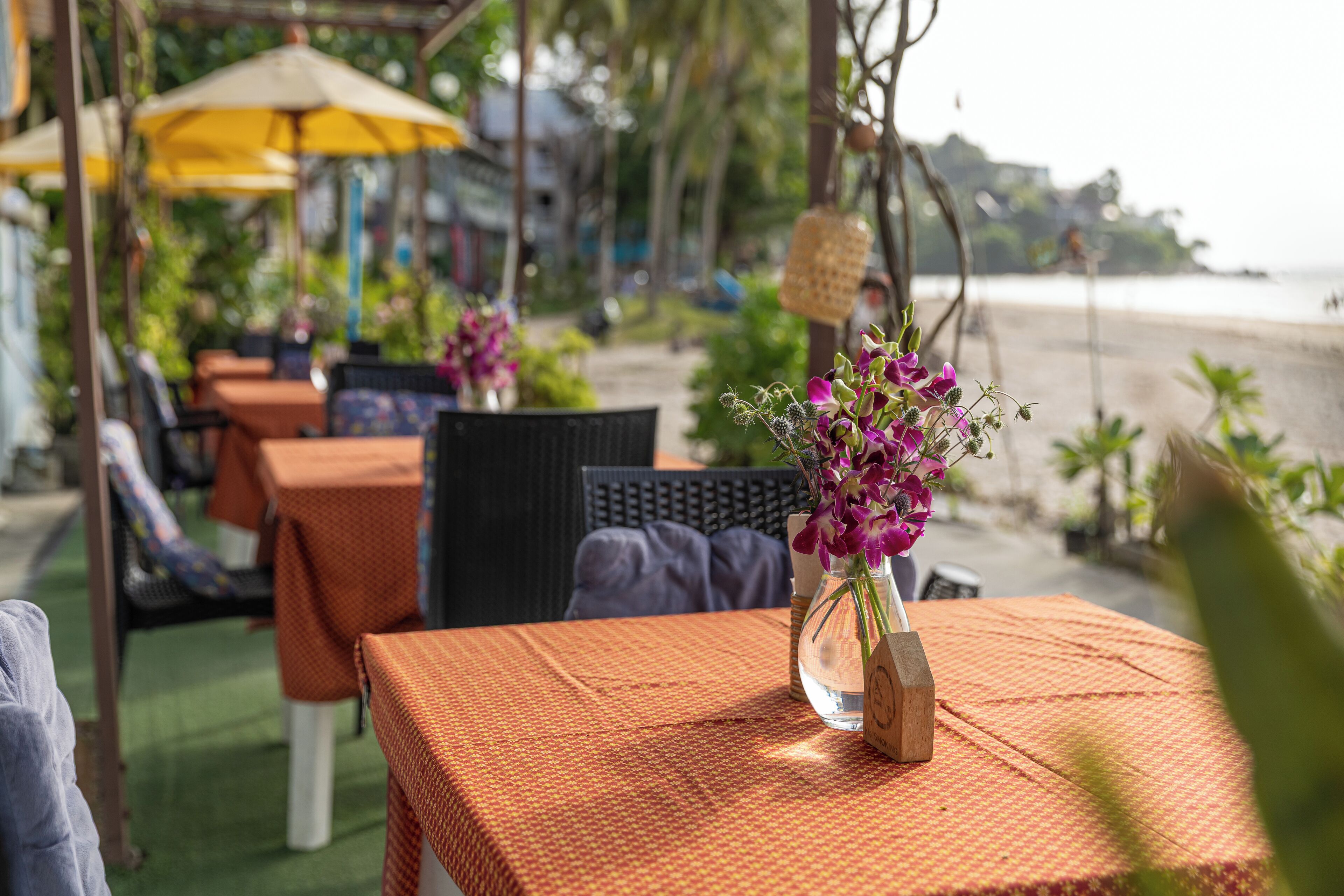 Un espace extérieur aménagé avec des tables recouvertes de nappes orange, des chaises et des parasols.