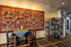 A room with a large carved wall, a table with chairs, and a bookshelf.