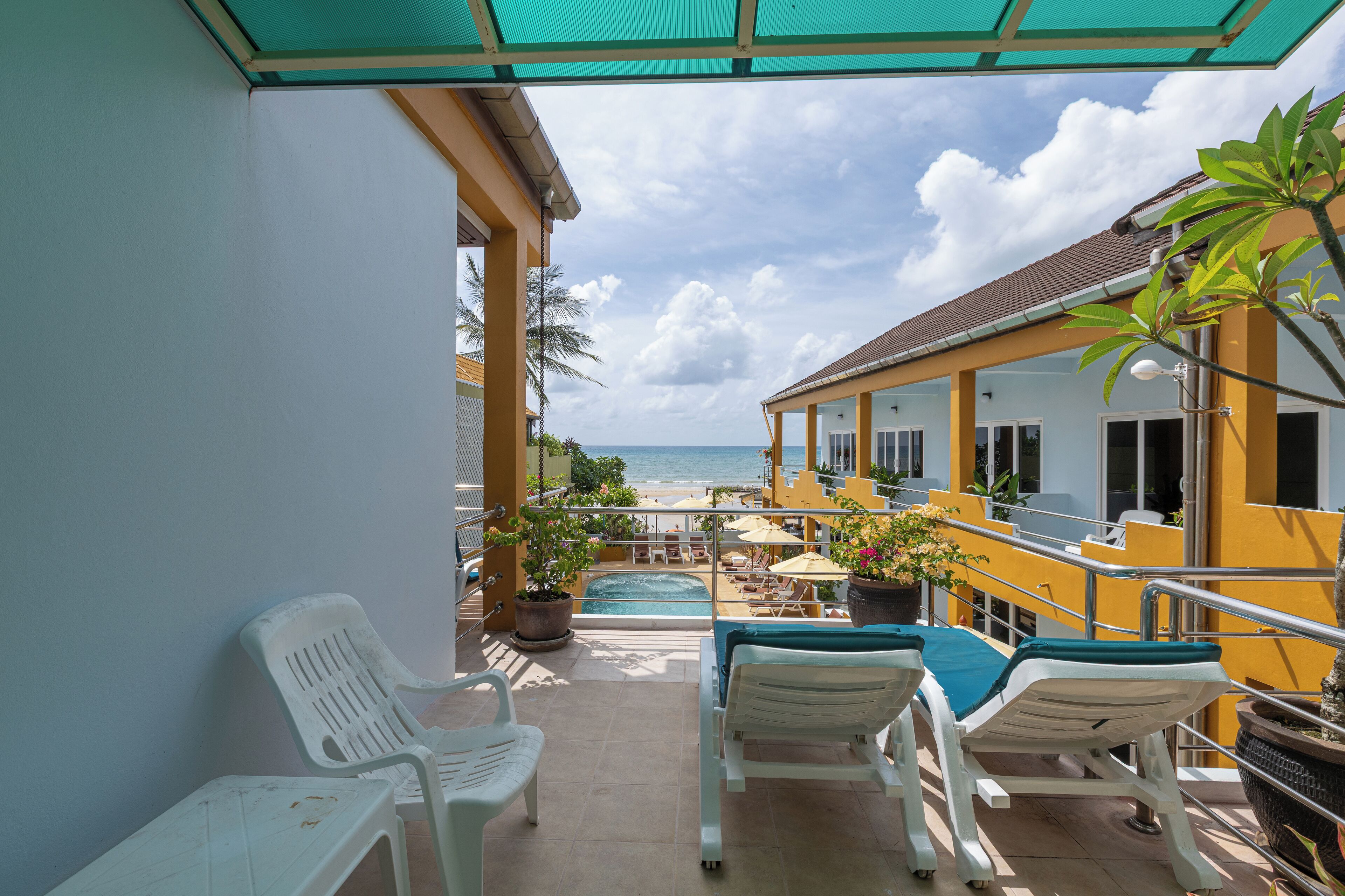 A balcony with white plastic chairs, a small pool, and a view of the beach.