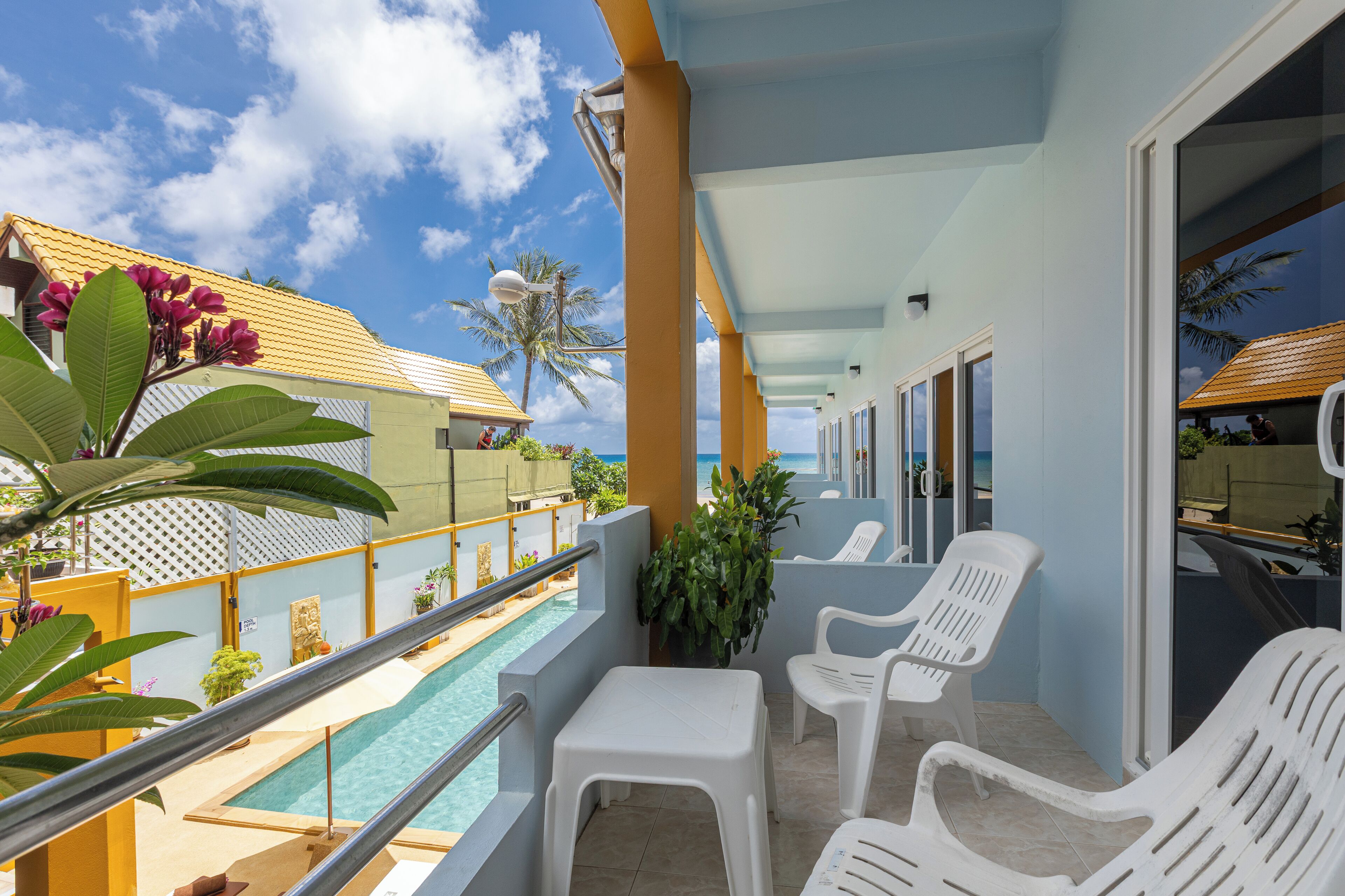 A balcony with white plastic chairs, a pool, and a view of the ocean.