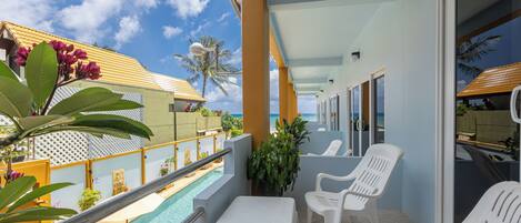 A balcony with white plastic chairs, a pool, and a view of the ocean.