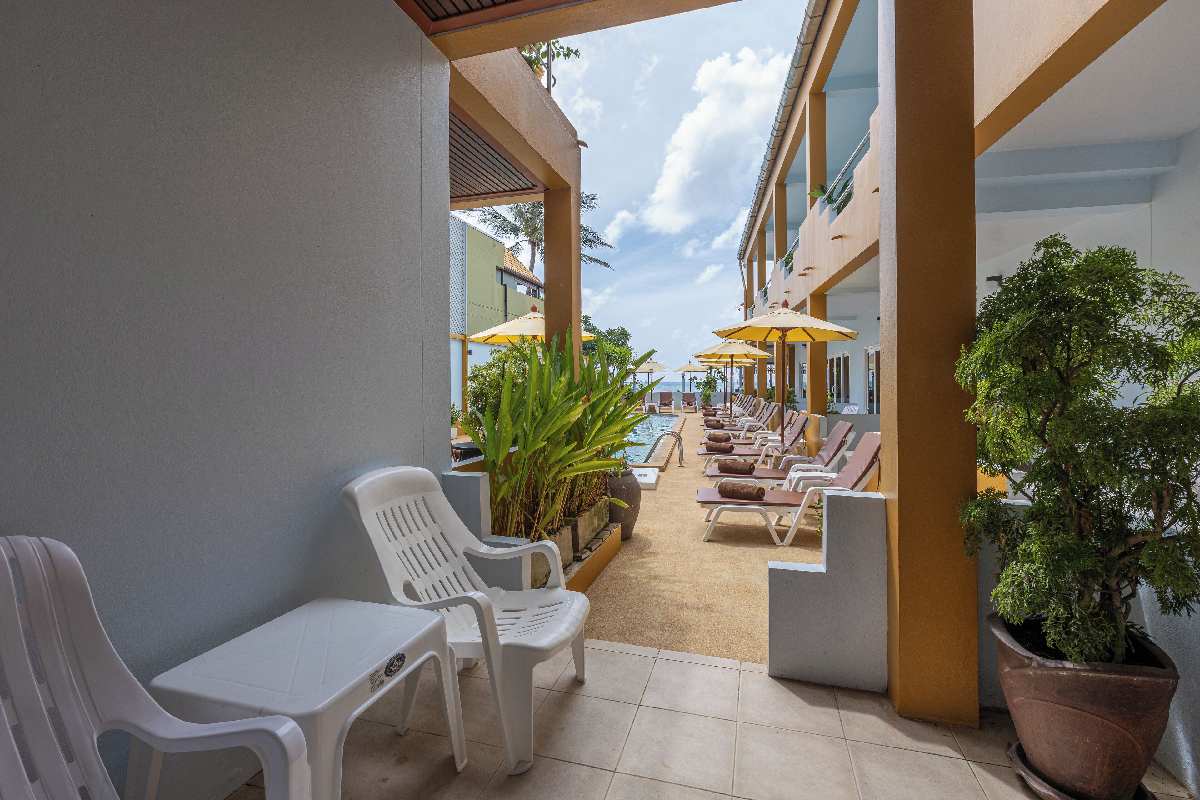 Un espace extérieur abrité, avec des chaises et des tables en plastique blanc, des parasols jaunes et une plante en pot.