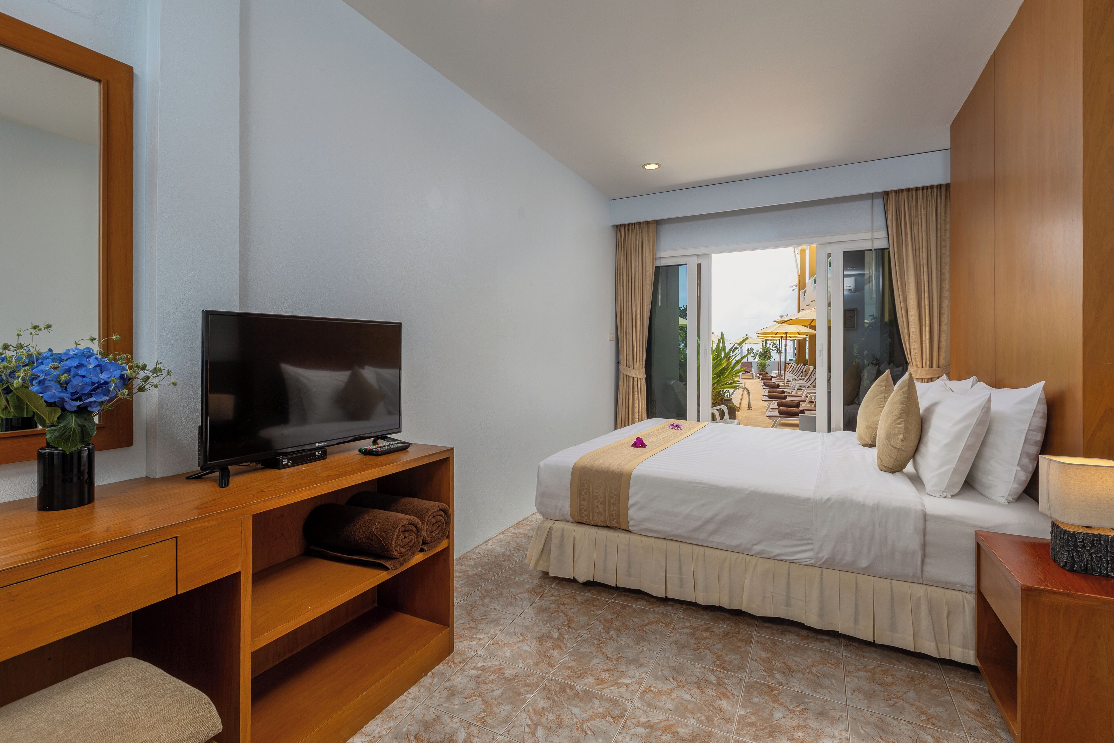 A hotel room with a bed, a TV, a desk, and a view of the outside.