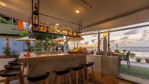 A bar area with a view of the sea, bar stools, and a variety of bottles on the shelves. - Kamala Dreams (Kamala)