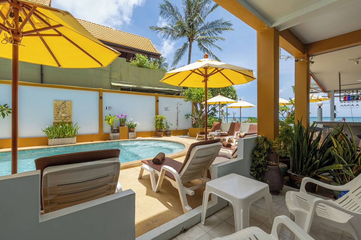 A poolside area with lounge chairs and yellow umbrellas, surrounded by potted plants and a view of the sea.