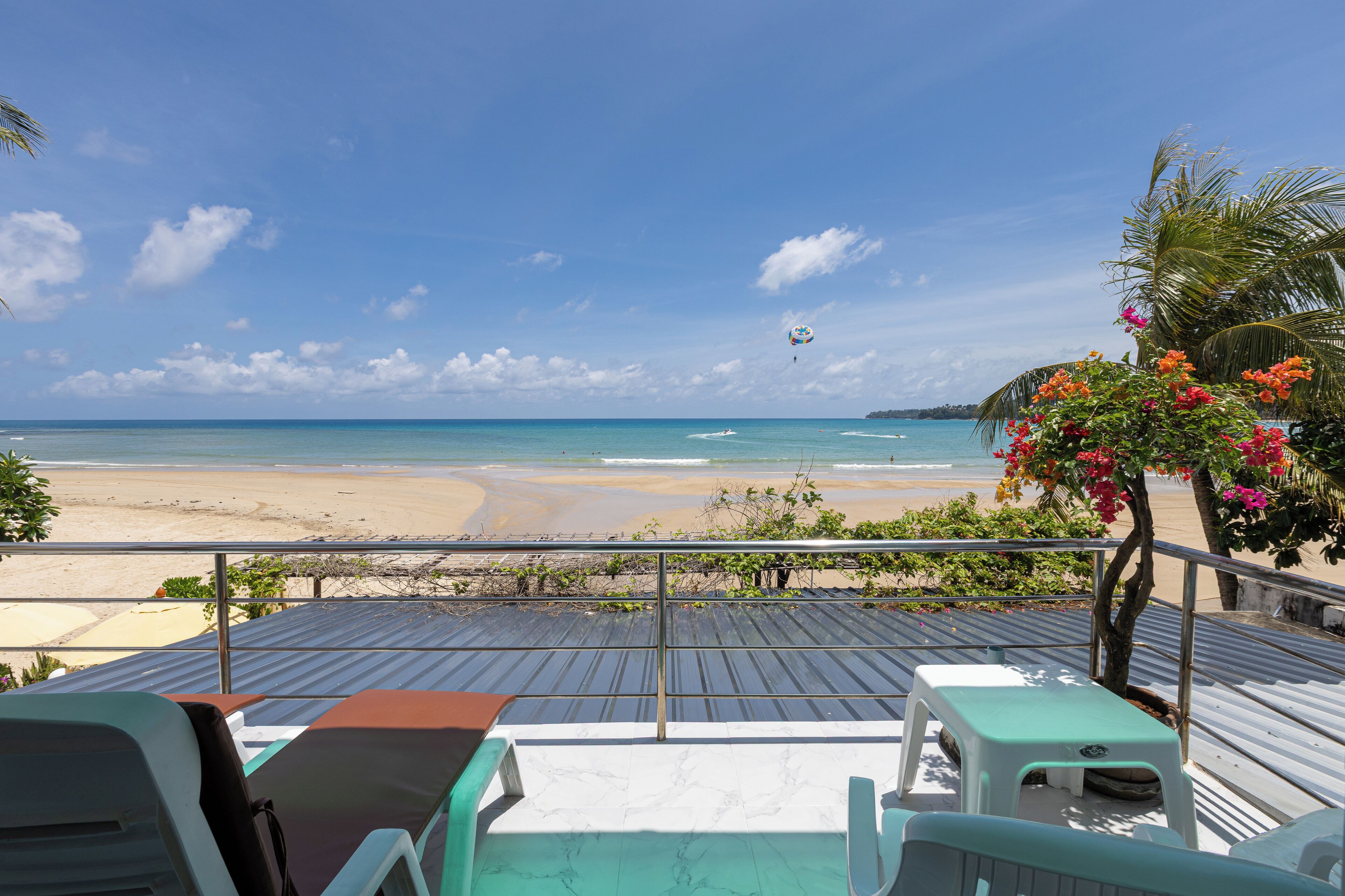 A beach view from a covered deck with lounge chairs and a table, overlooking the ocean.