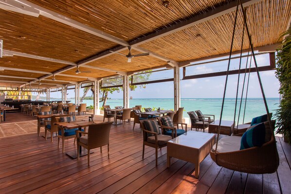 A covered outdoor seating area with wooden flooring and wicker furniture, overlooking a body of water. - Chaweng Regent Beach Resort (Koh Samui)