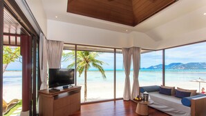 Un salon spacieux doté d’un grand téléviseur, d’un meuble en bois et d’un canapé placé face à de grandes fenêtres offrant une vue sur la plage.