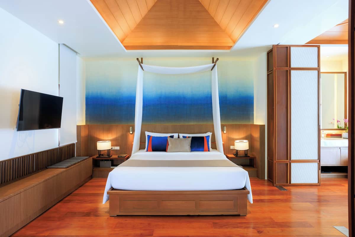 Una habitación de hotel moderna con una cama grande, cabecera de madera, lámparas de noche, un televisor de pantalla plana y un ventanal con vistas.