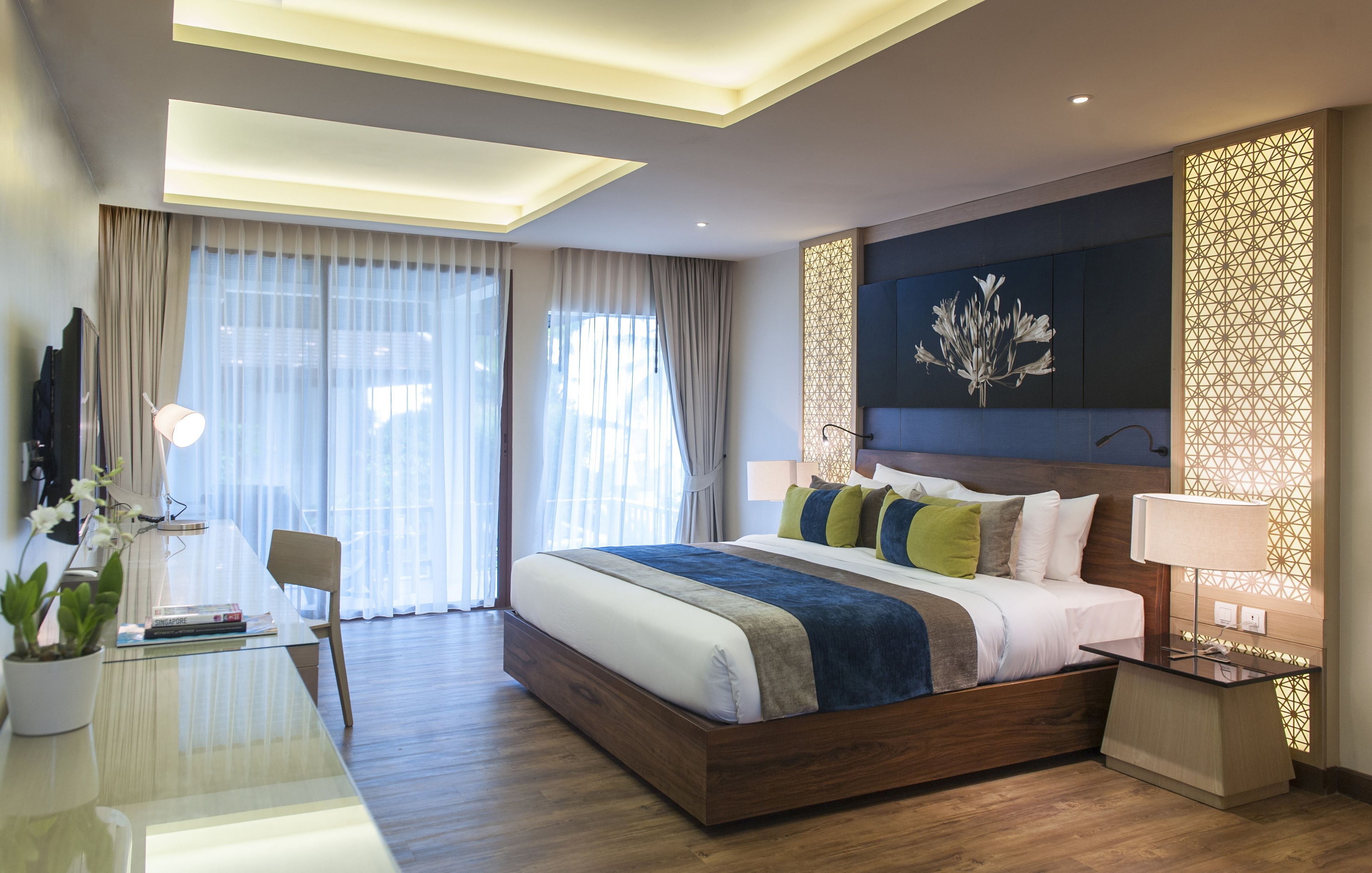 A modern hotel room with a large bed, a desk with a lamp, and a decorative wall panel.