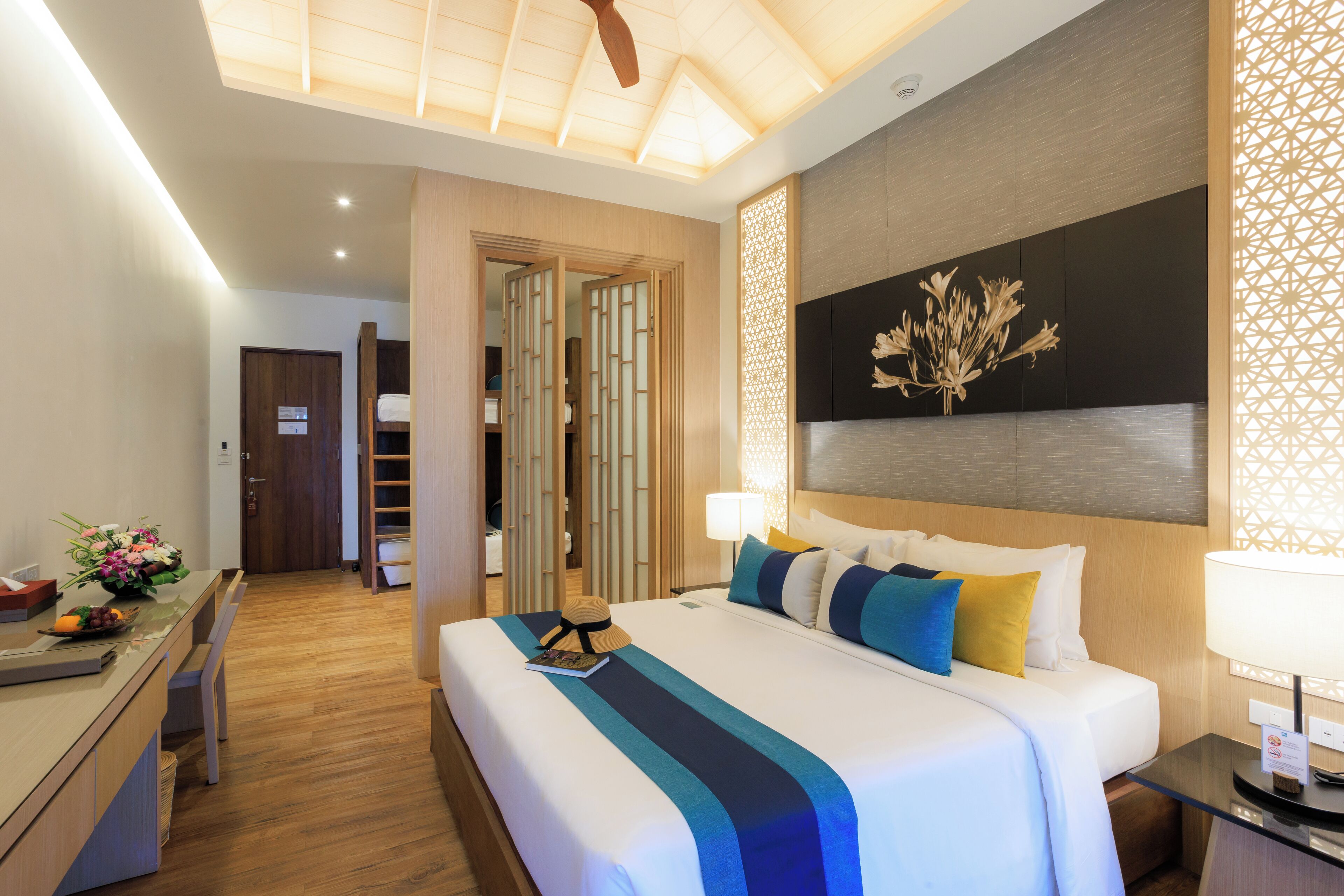 Ein Hotelzimmer mit einem großen Bett, einem Nachttisch und einem Schreibtisch mit Stuhl. Eine Tür führt in einen anderen Raum.